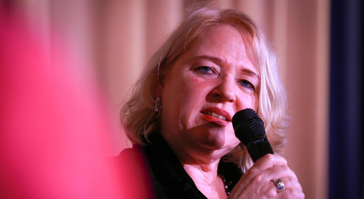  A woman with blond hair speaks into a microphone.