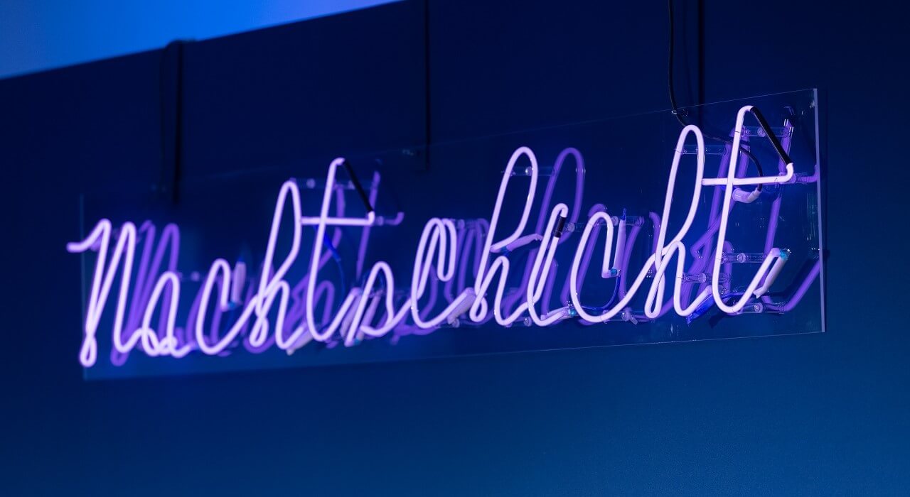 Illuminated lettering Nachtschicht on dark blue background.