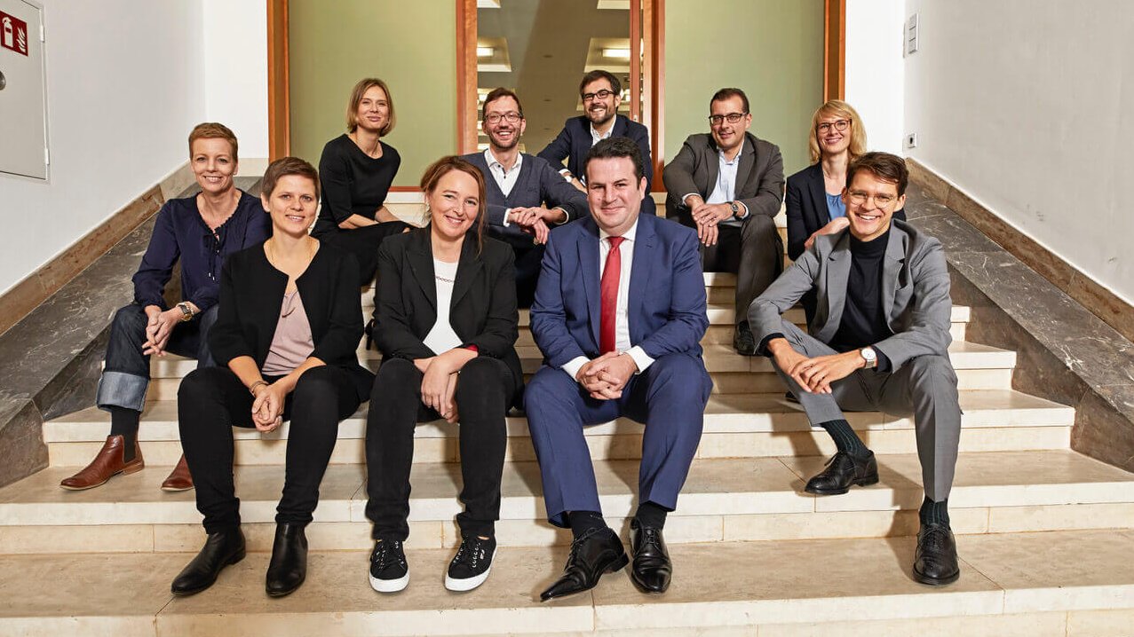 Federal Minister of Labor Hubertus Heil and nine other people sit on a staircase and smile.