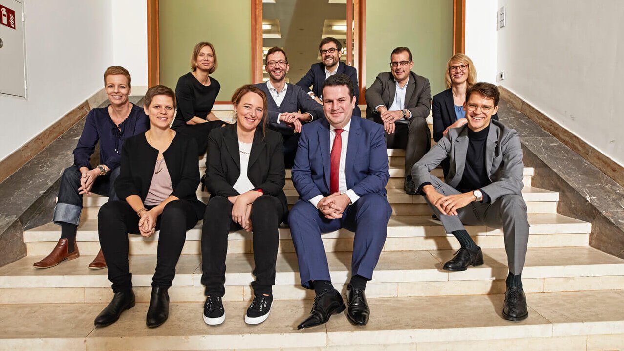 Bundesarbeitsminister Hubertus Heil und neun weitere Personen sitzen auf einer Treppe und lächeln