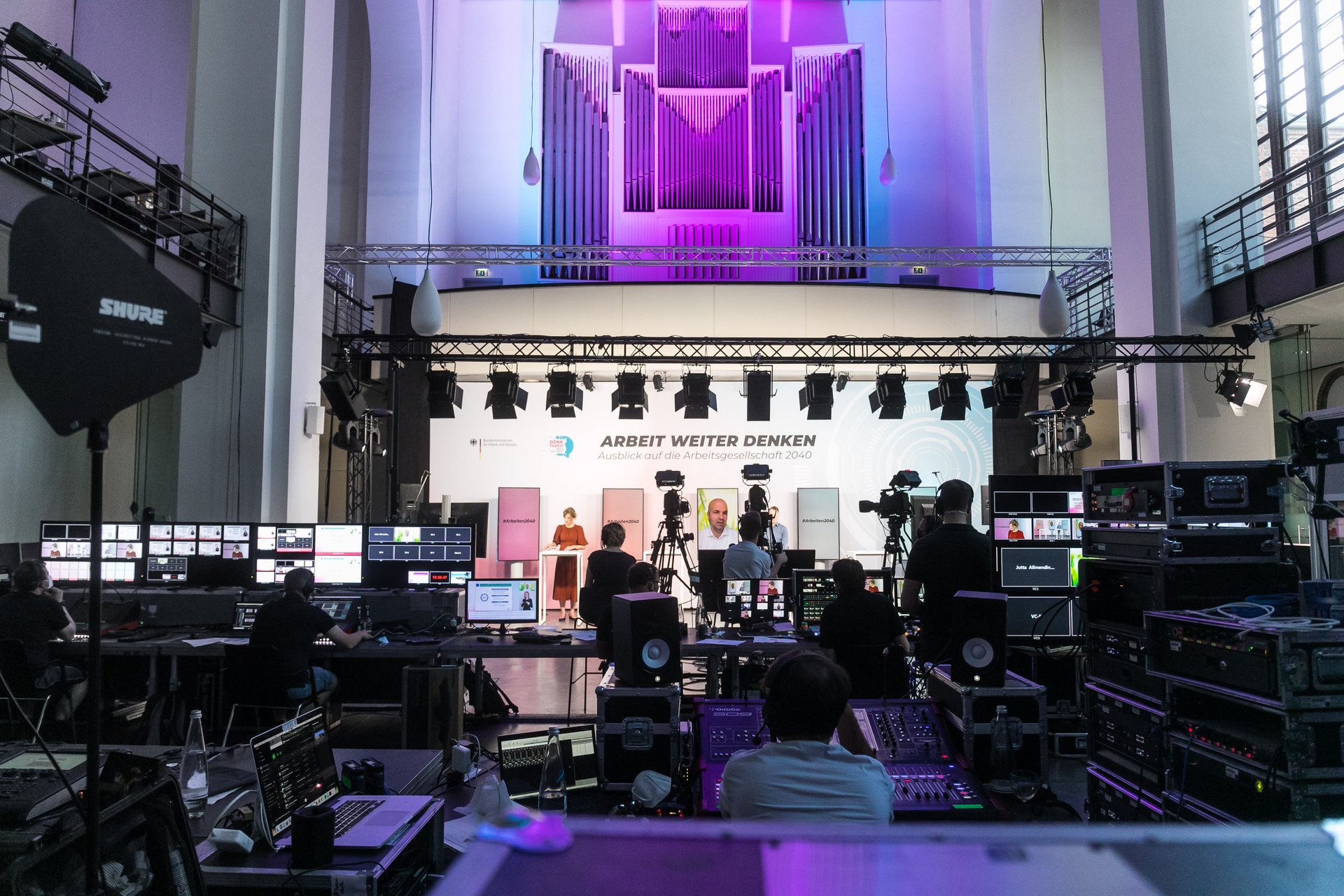 Vor einer Bühne, die von mehreren Kameras aufgezeichnet wird, befindet sich die Übertragungs- und Veranstaltungstechnik.