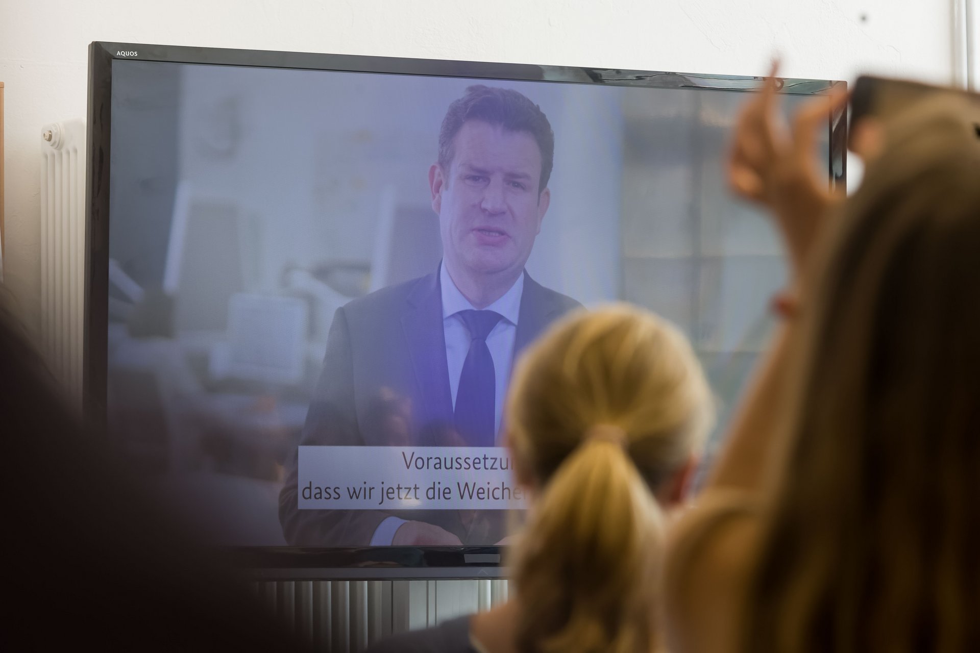 Bundesminister Hubertus Heil spricht in einer Videobotschaft, die auf einem Bildschirm ausgespielt wird.