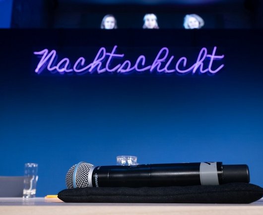 A microphone on the podium with the lettering Nachtschicht in the background.